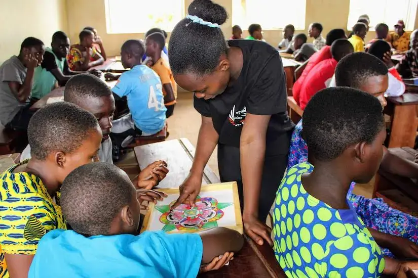 Tisiya Mahoro, with My HOME Stars, helping students play the 5 STA-Z board game at Kinakyeitaka Primary School