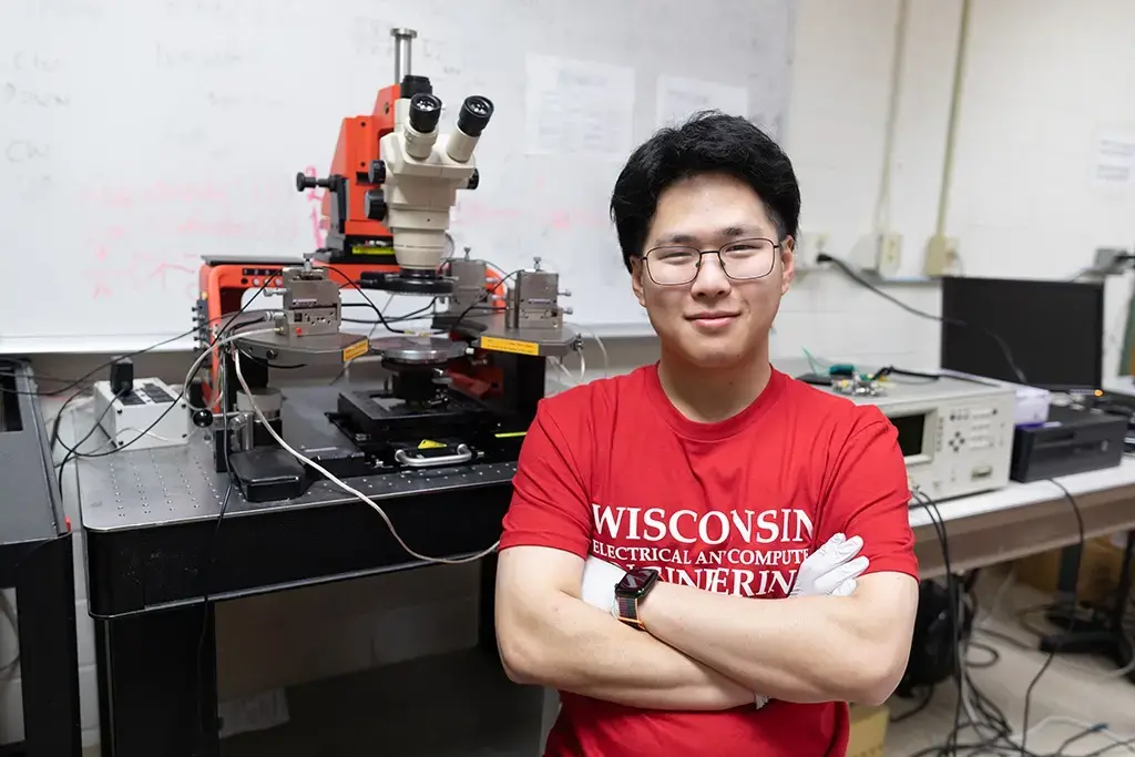 Student stands at lab table with equipment where light emitting diodes (LEDs) and LASERs use Gallium Nitride and its alloys to produce Ultraviolet, visible and Infrared light