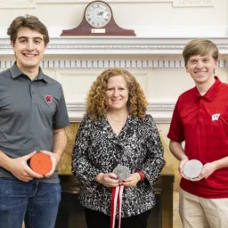 students Teekay Kowalewski (left) and Dylan Zinkgraf (right) present Chancellor Jennifer L. Mnookin with the medallion