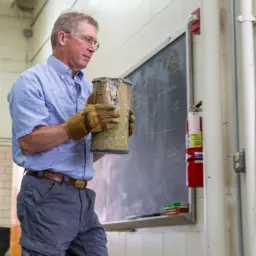 Steven Cramer, a civil and environmental engineering professor emeritus, carries a fractured concrete sample after testing it in a hydraulic press.