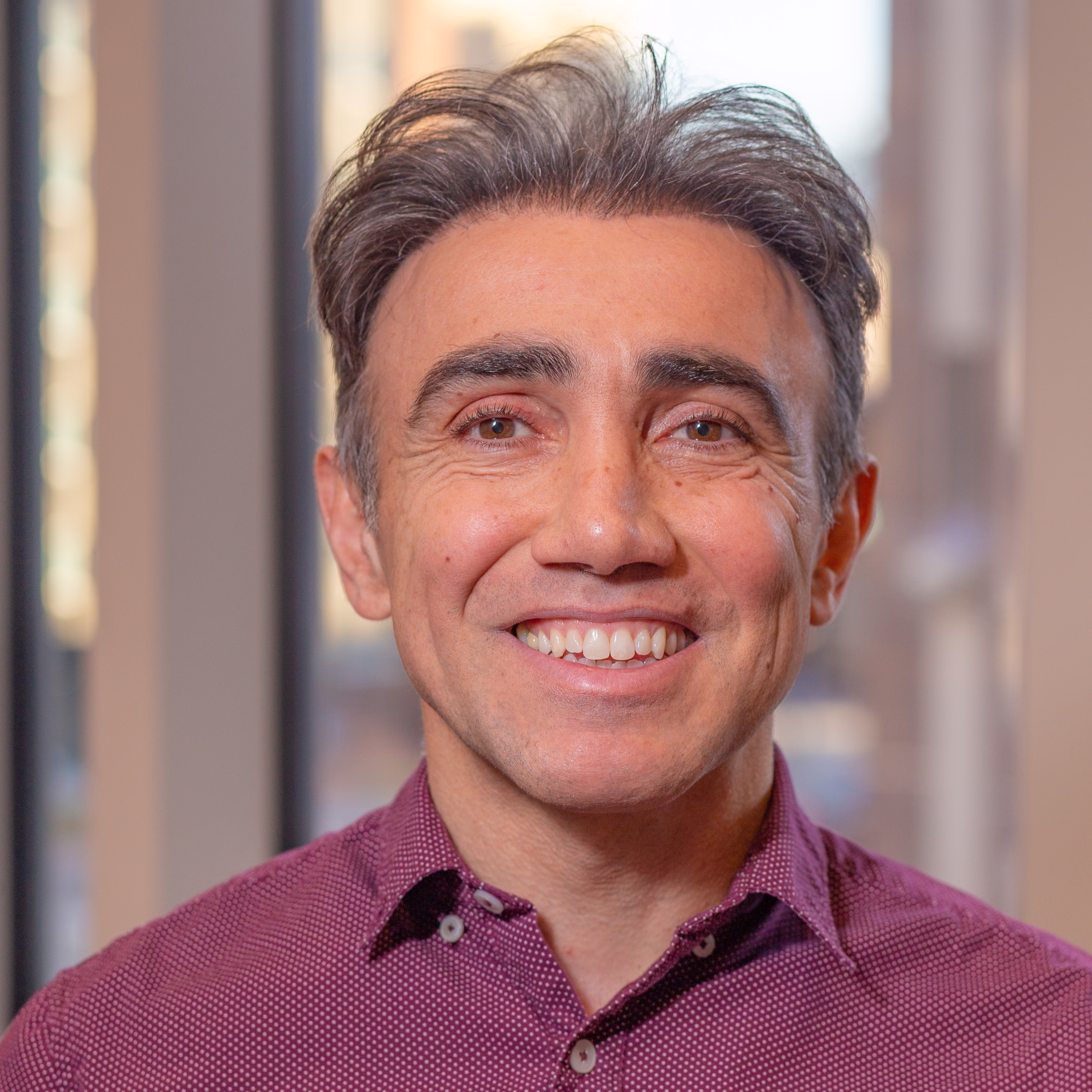 Mid-career man with graying hair and brown eyes, smiling, wearing a burgundy polka-dot collared shirt