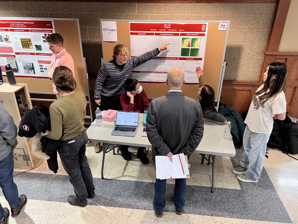 Two students pointing to research poster on bulletin board with alumni judge looking on